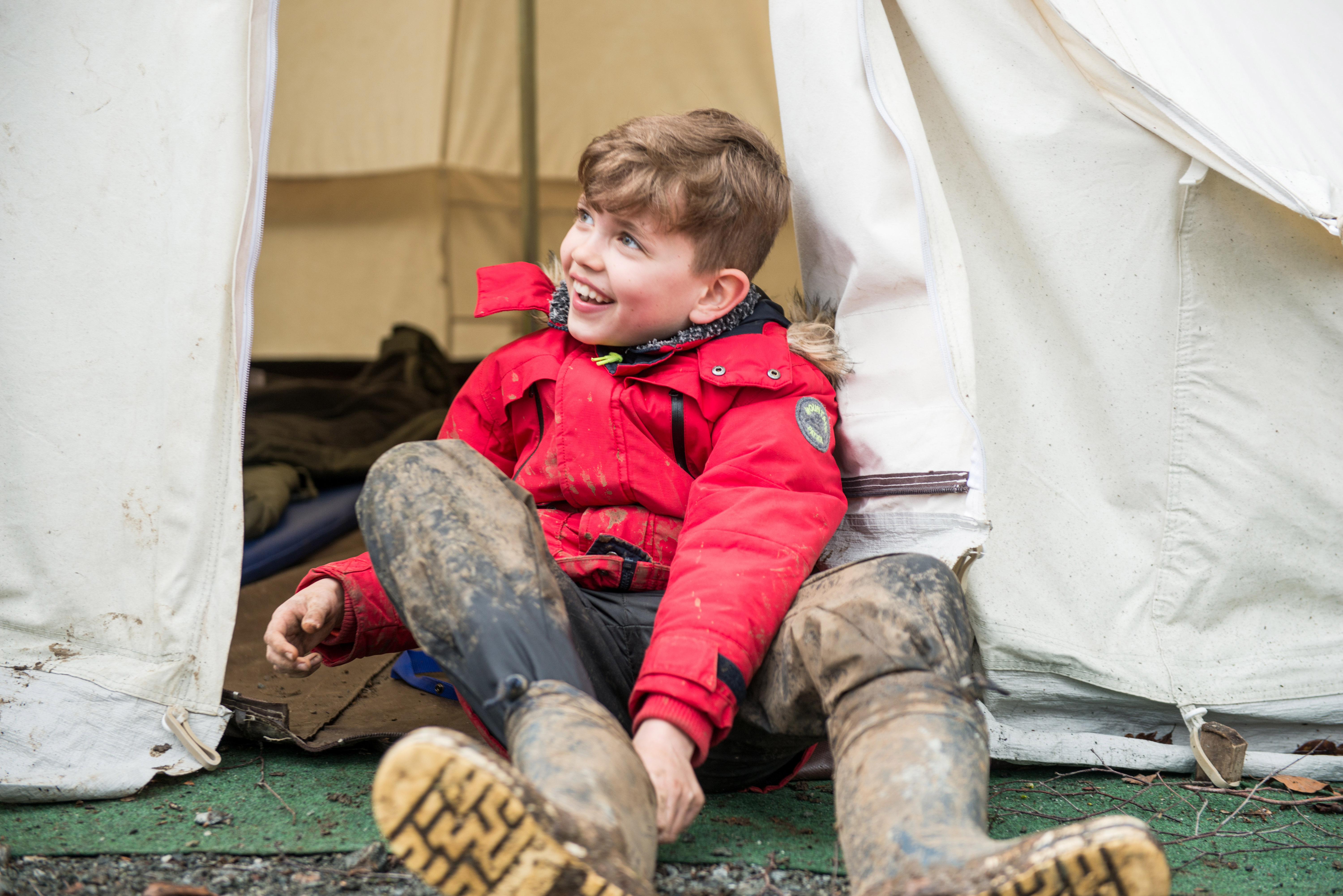 Boy puts on boots outside tent